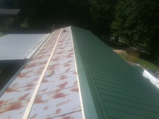 Old rusted panels beside newly installed green metal roofing — Wind Damage Roof Repair by Roofing Brothers in Manson