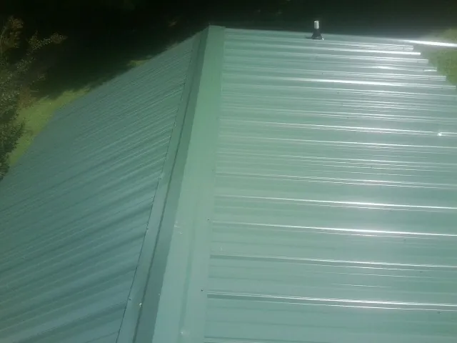 New green metal panels meeting at the ridge of a roof — Flat Roof Repair work by our crew in Manson
