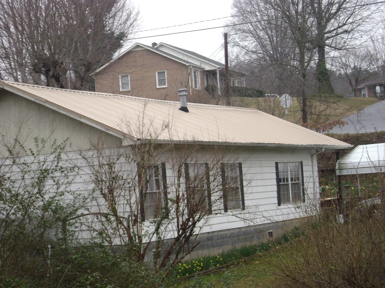 Tan metal roof on a white sided house set into a hillside — Commercial Roofing by Roofing Brothers in Manson